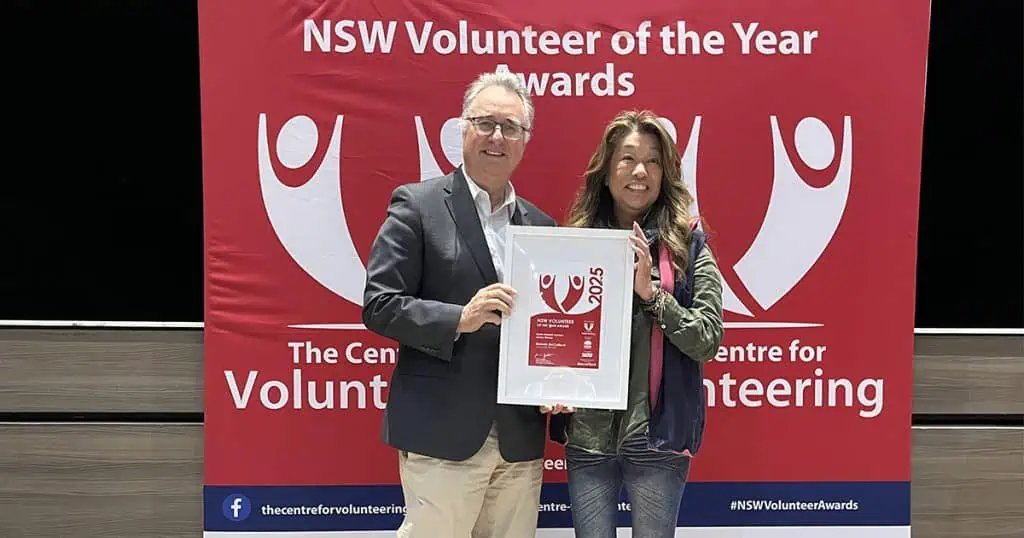 Two individuals holding NSW Volunteer of the Year award at a formal event.